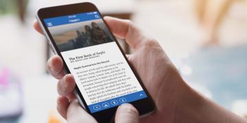 A woman holds up a smartphone with the ScripturePlus app open to 1 Nephi 1. A woman holds up a smartphone with the ScripturePlus app open to 1 Nephi 1.